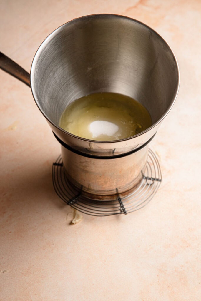 A mixing bowl with eggs and sugar on top of a pan. Double boiler.