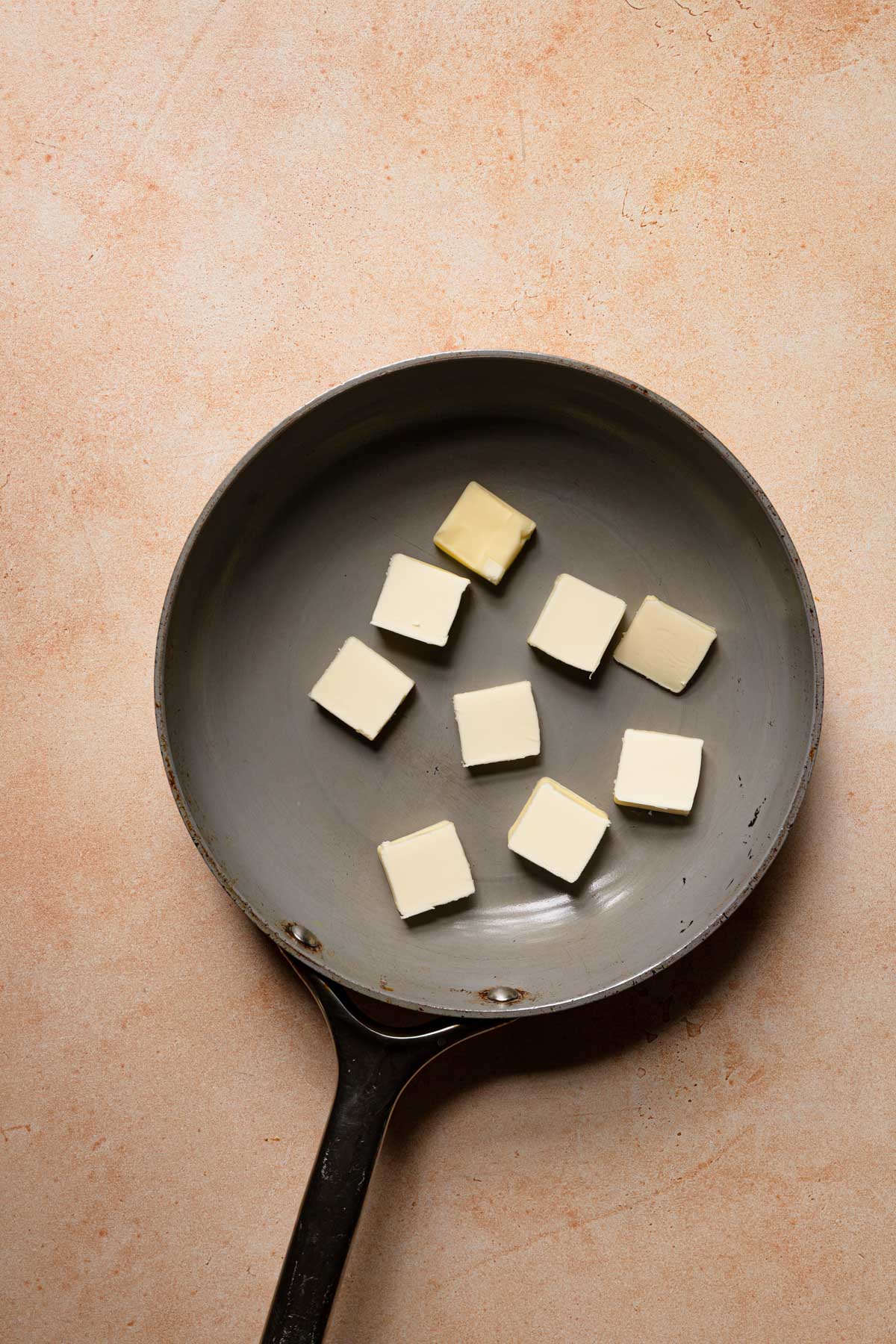 A wide skillet with butter pieces.