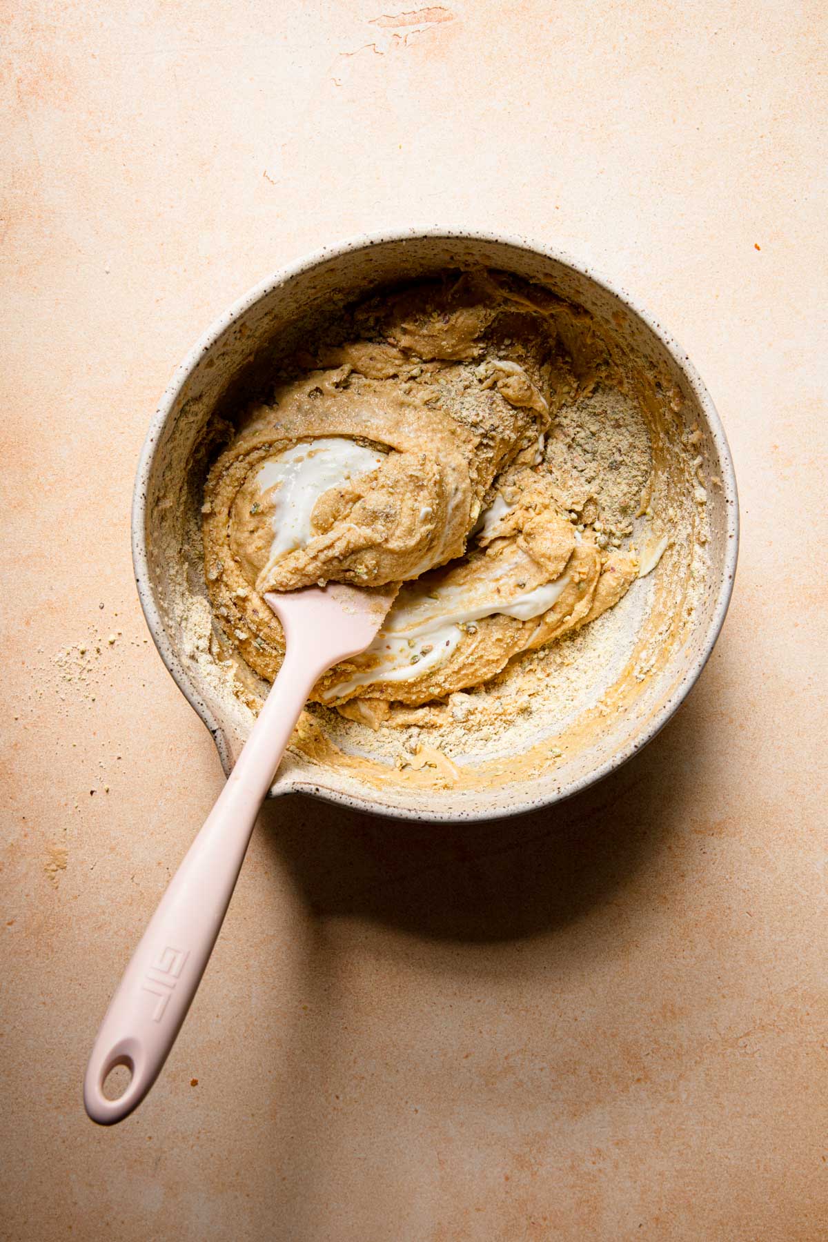 A mixing bowl with a cake butter folding cream with a spatula.
