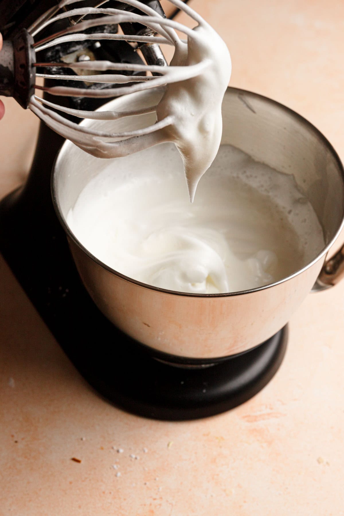 A stand mixer with a bowl full of meringue and a whisk with the meringue dripping.