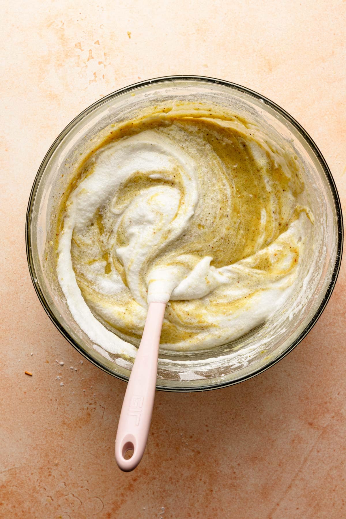 A bowl with meringue folded into batter and a spatula.