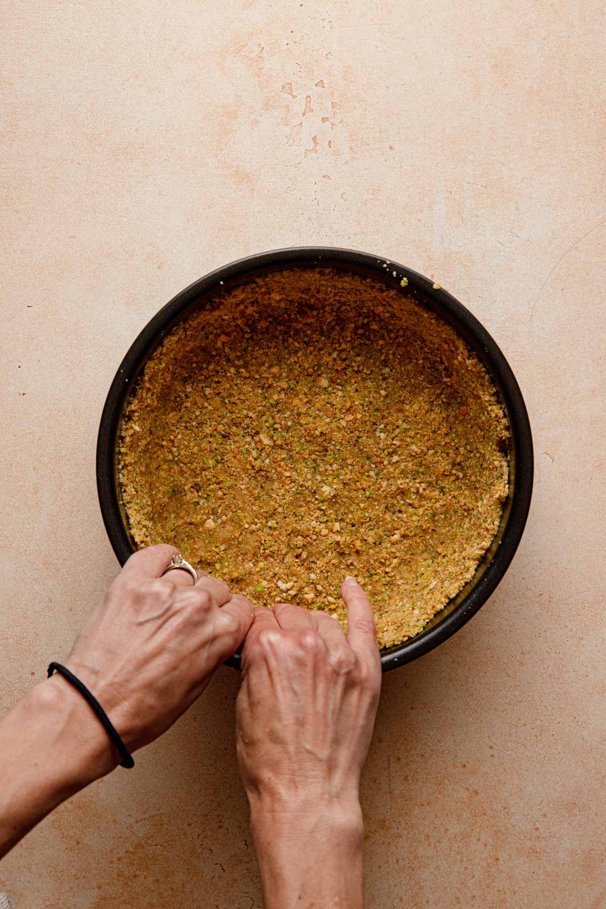 Hands pressing pistachio crumbs into a crust.