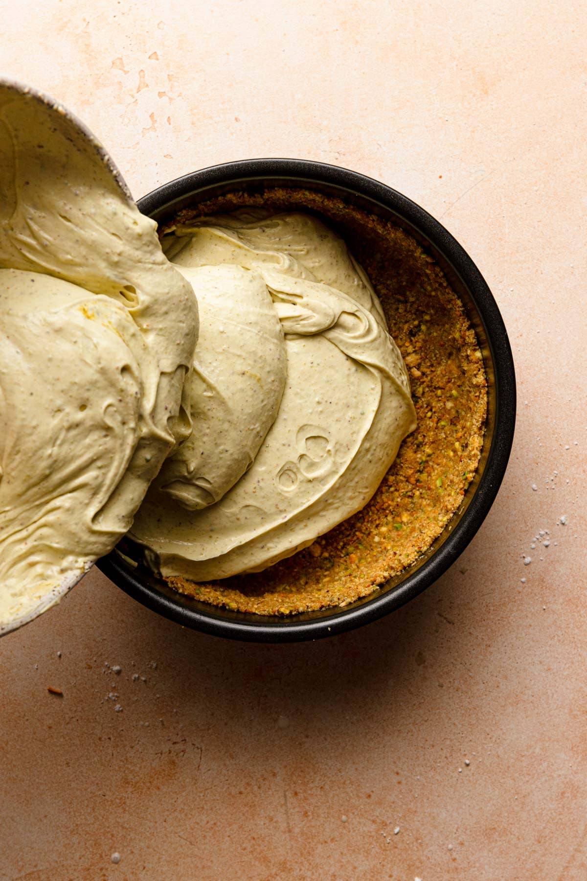 Pouring pistachio cheesecake batter into a pan lined with crust.