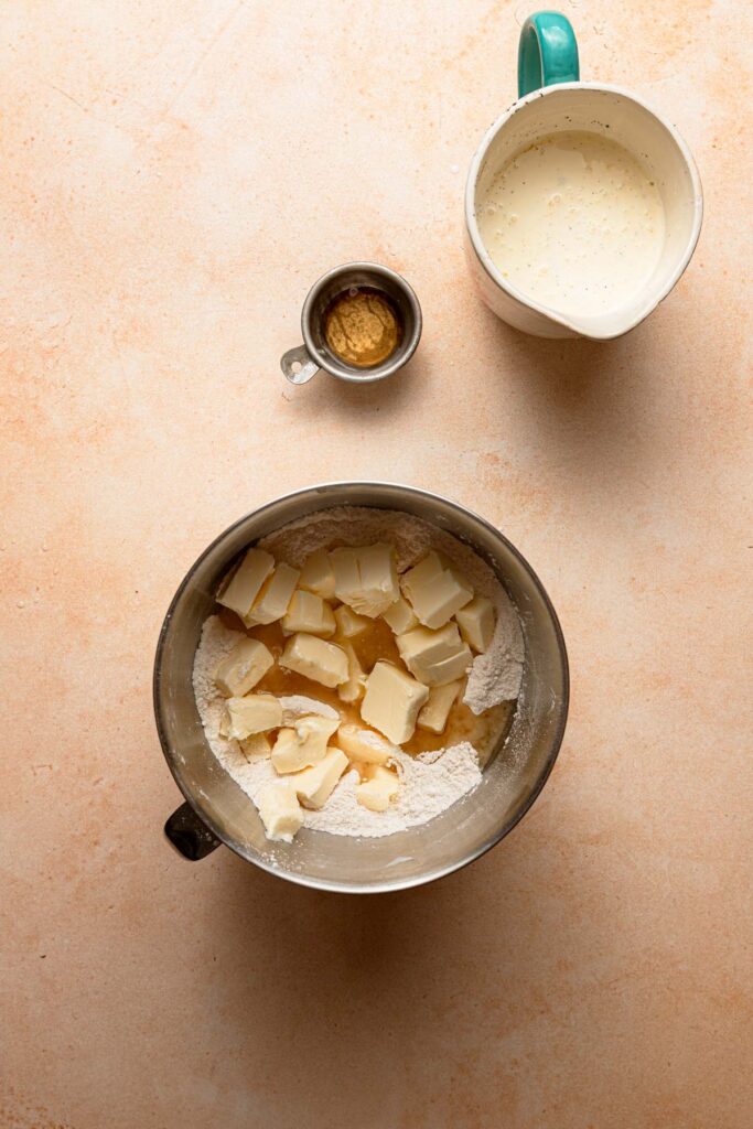 A mixing bowl with flour and butter. A small bowl with apple cider vinegar. A large cup with heavy cream.