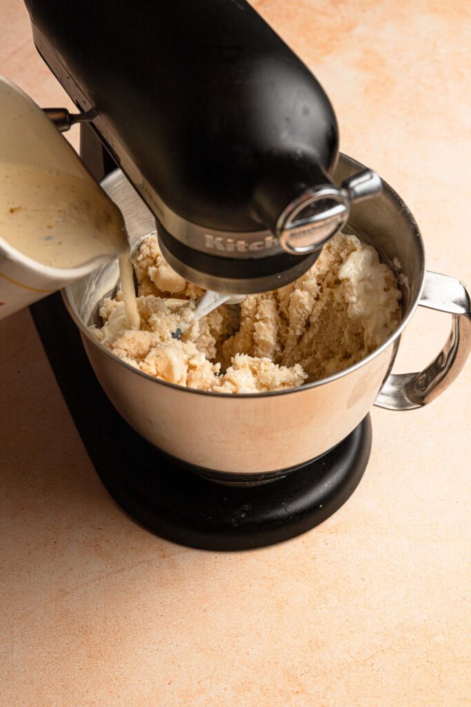 Pouring liquid into a bowl of a stand mixer full of flour mixture.