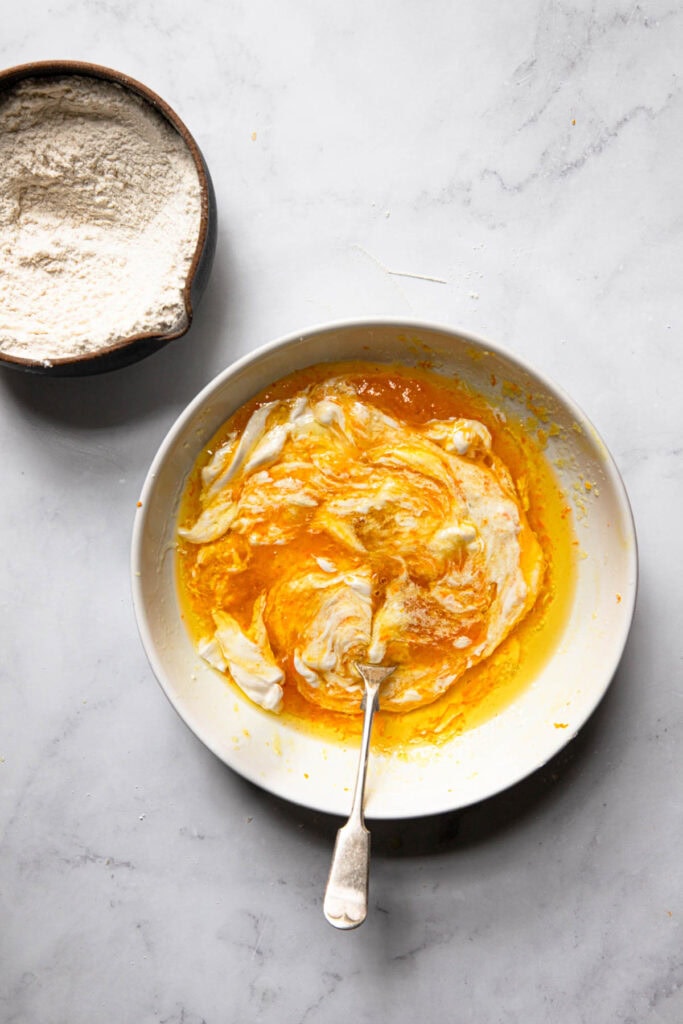 A bowl with orange sugar, oil and sour cream next to a bowl with flour mixture.