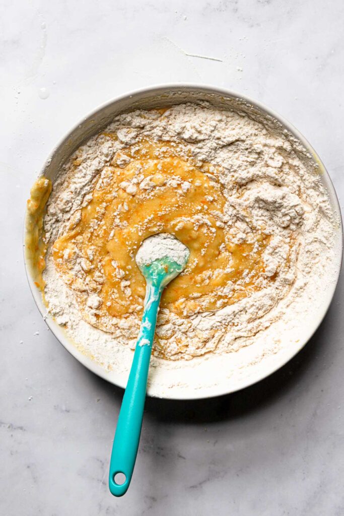 A bowl with a spatula mixing flour into a batter.