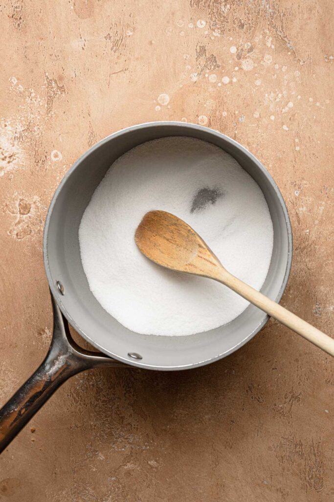 A sauce pan with sugar and a wooden spoon.