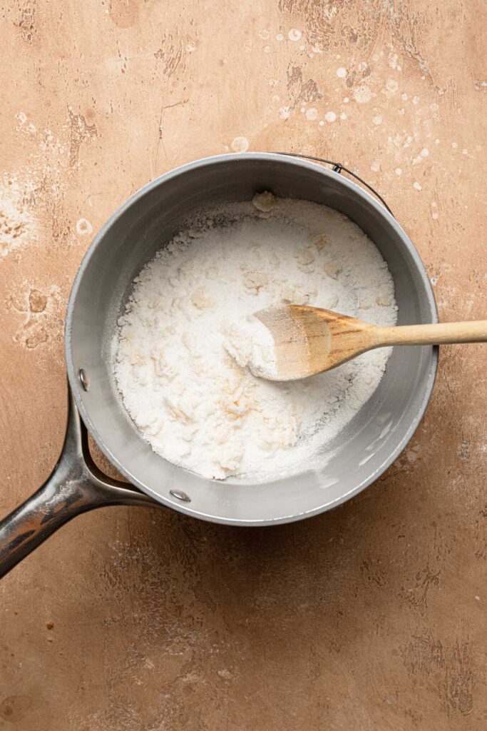 A sauce pan with some clump sugar and a wooden spoon.