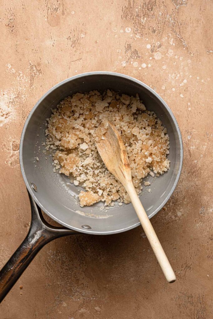 A sauce pan with clump sugar and a wooden spoon.