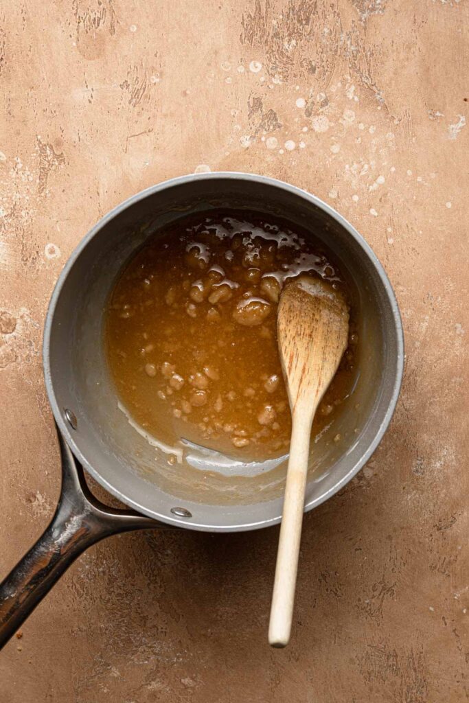 A sauce pan with caramel and some clump sugar and a wooden spoon.
