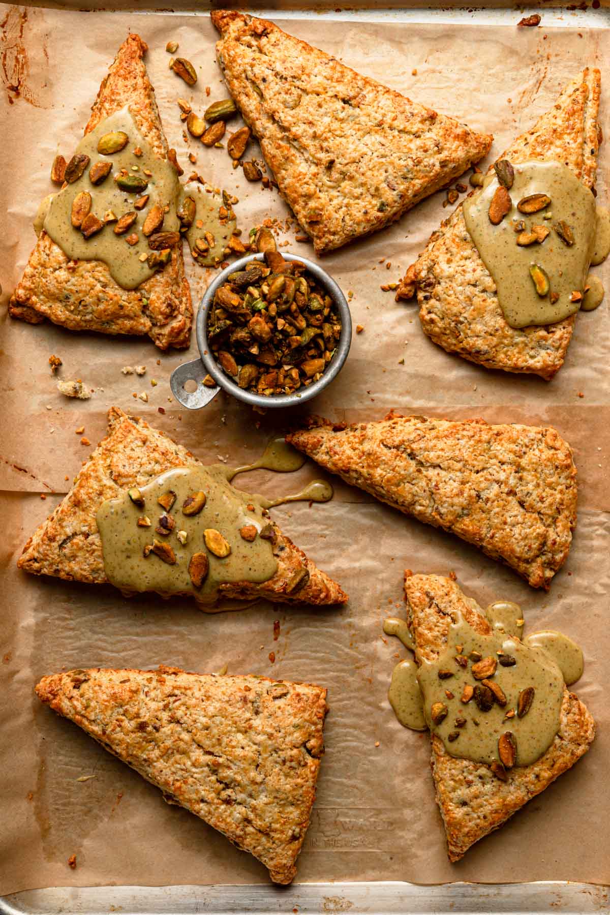 Pistachio scones on a pan glazed with pistachio glaze and sprinkle with chopped pistachios.