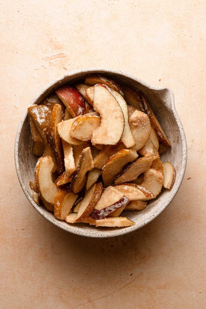 A bowl with sliced pears coated with sugar mixture.