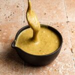 A spoon with pistachio glaze in a bowl.