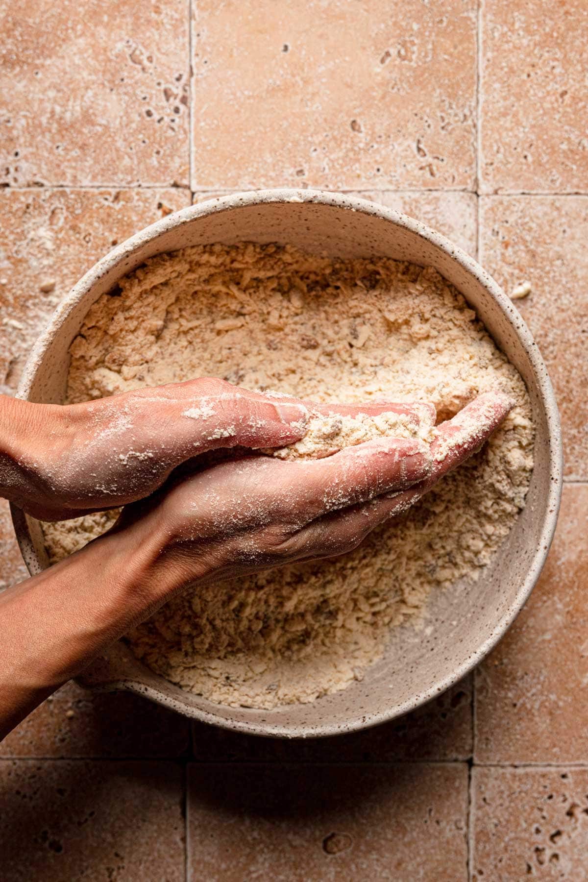 Hands rubbing butter into flour mixture for scones.