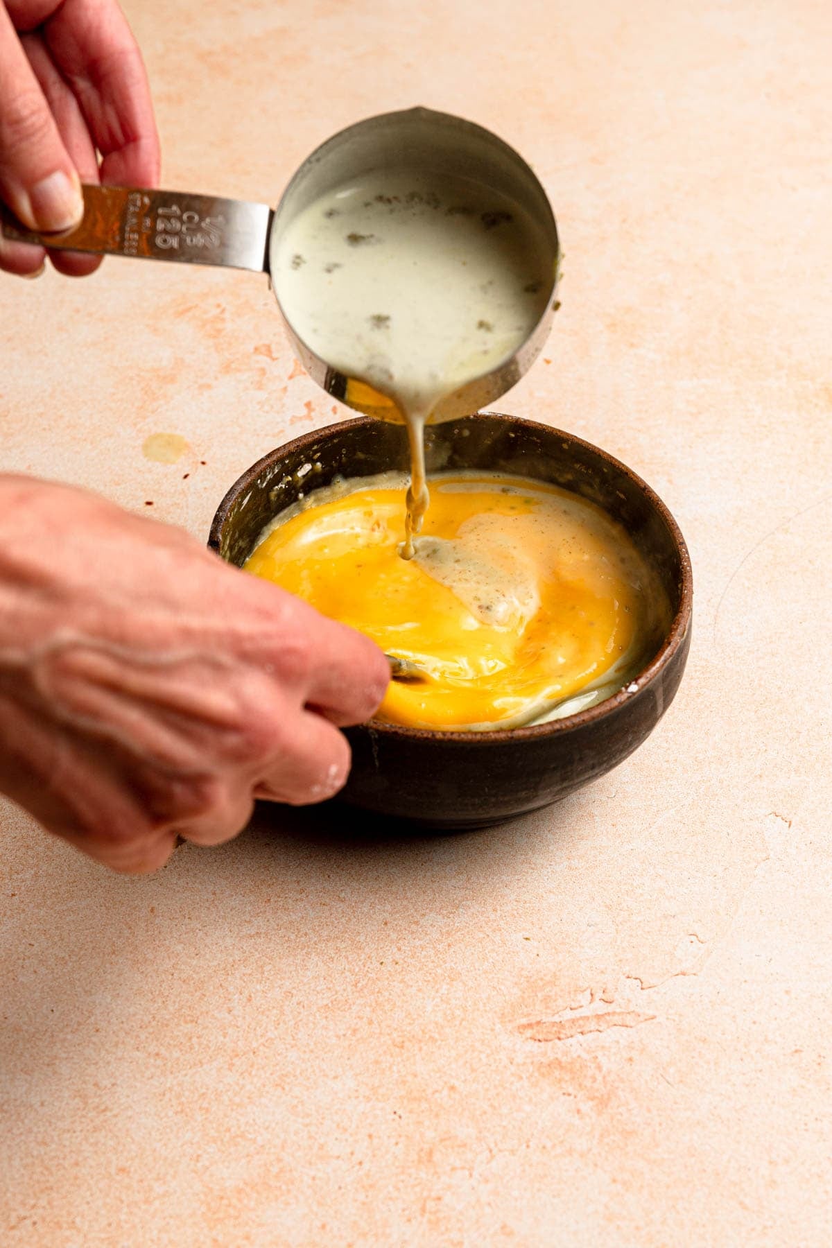 Pouring milk into a bowl with eggs while hand stirring.