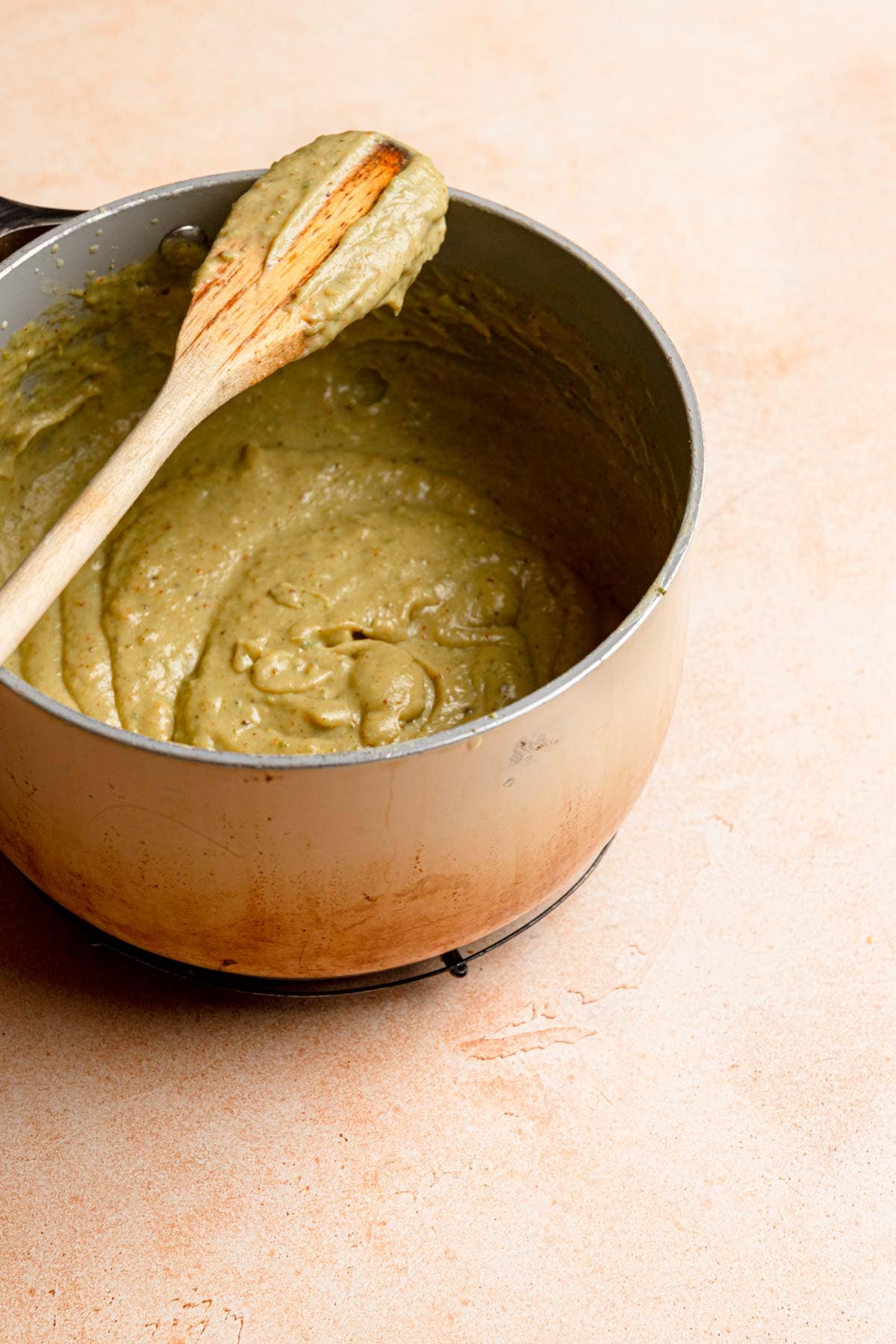 A saucepan with pistachio cream and a wooden spoon.