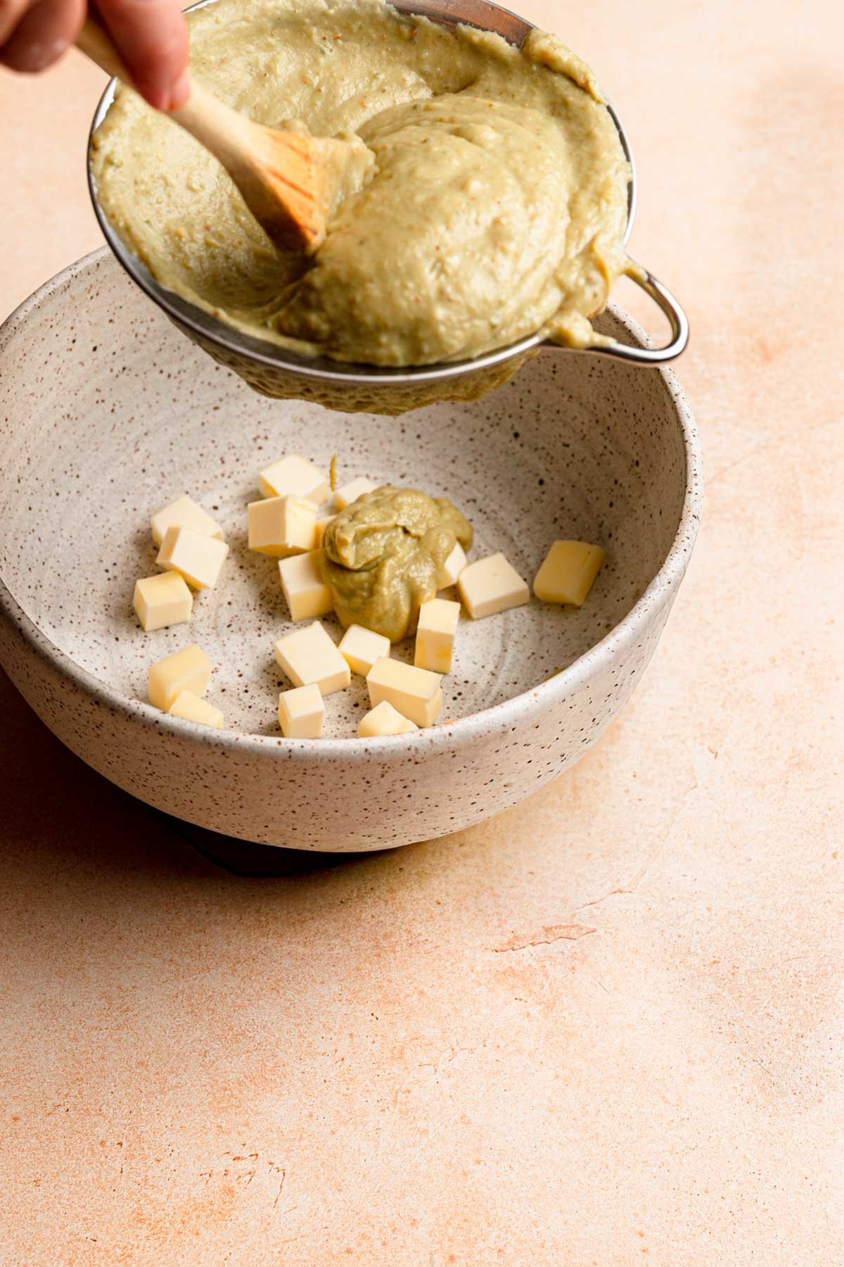 Running cream through a sieve into a bowl with pieces of butter in it.