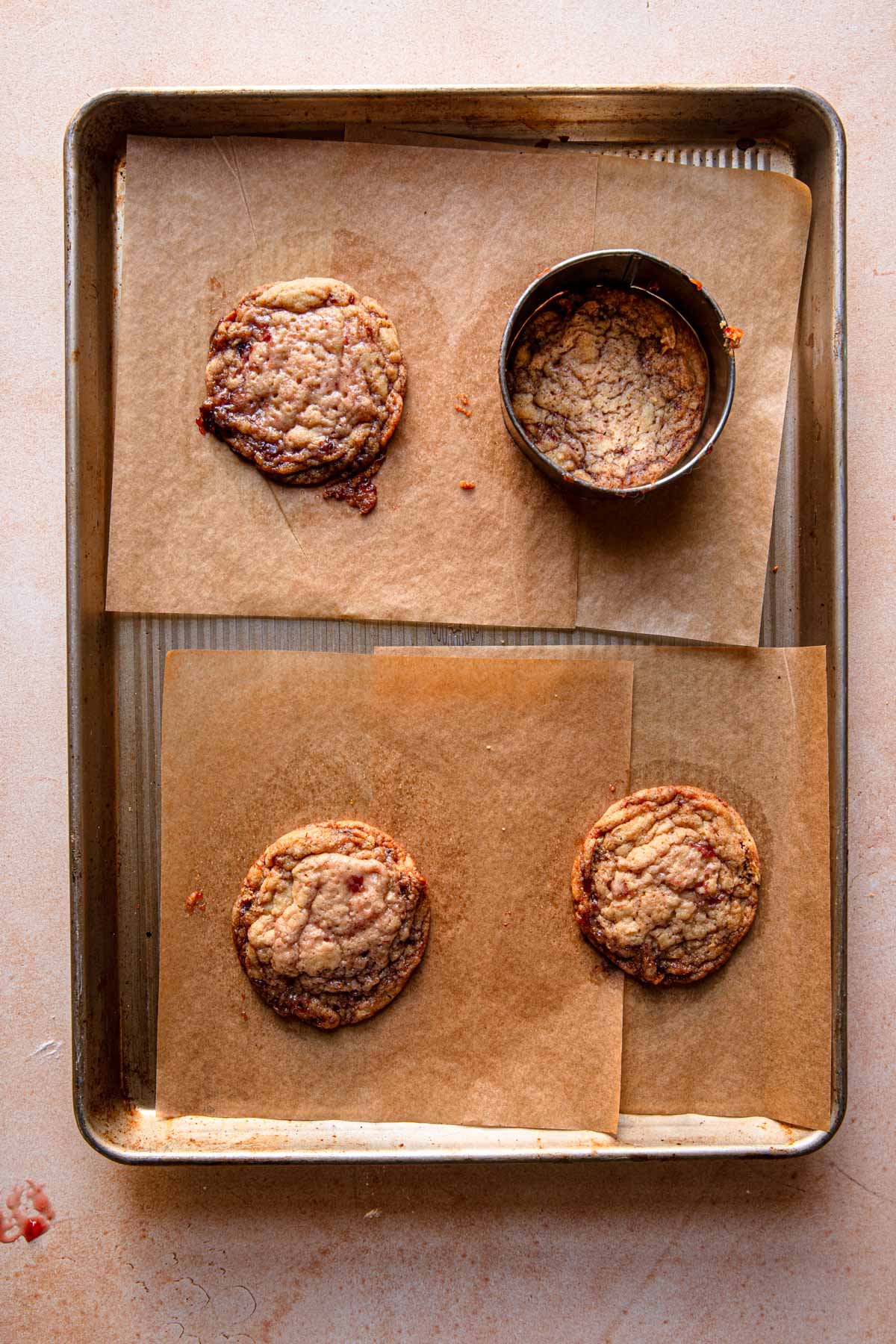 Cookies over a pan with parchment paper and a cookie cutter swirling one of the cookies.