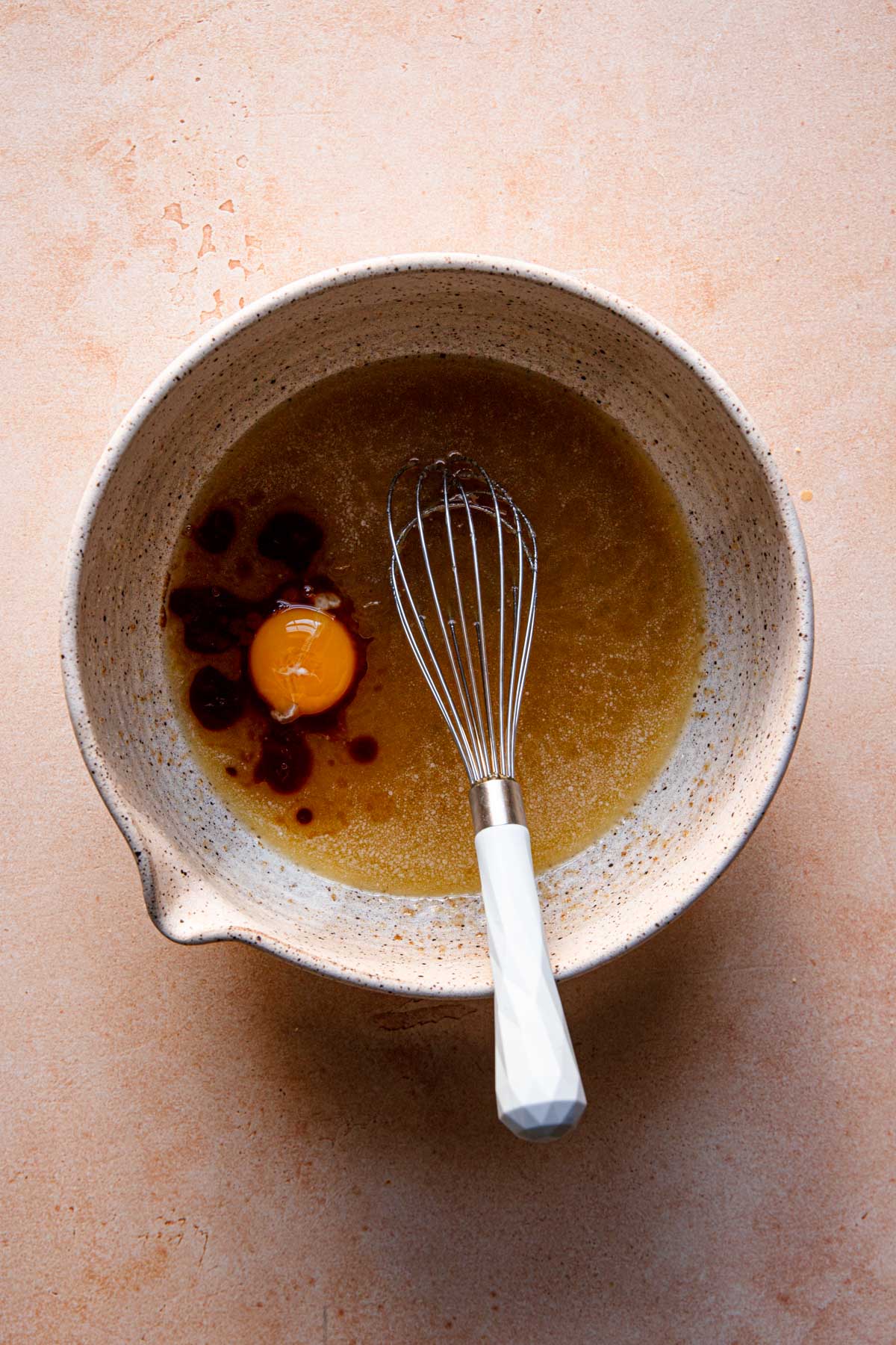 A large bowl with melted butter an egg yolk and a whisk.