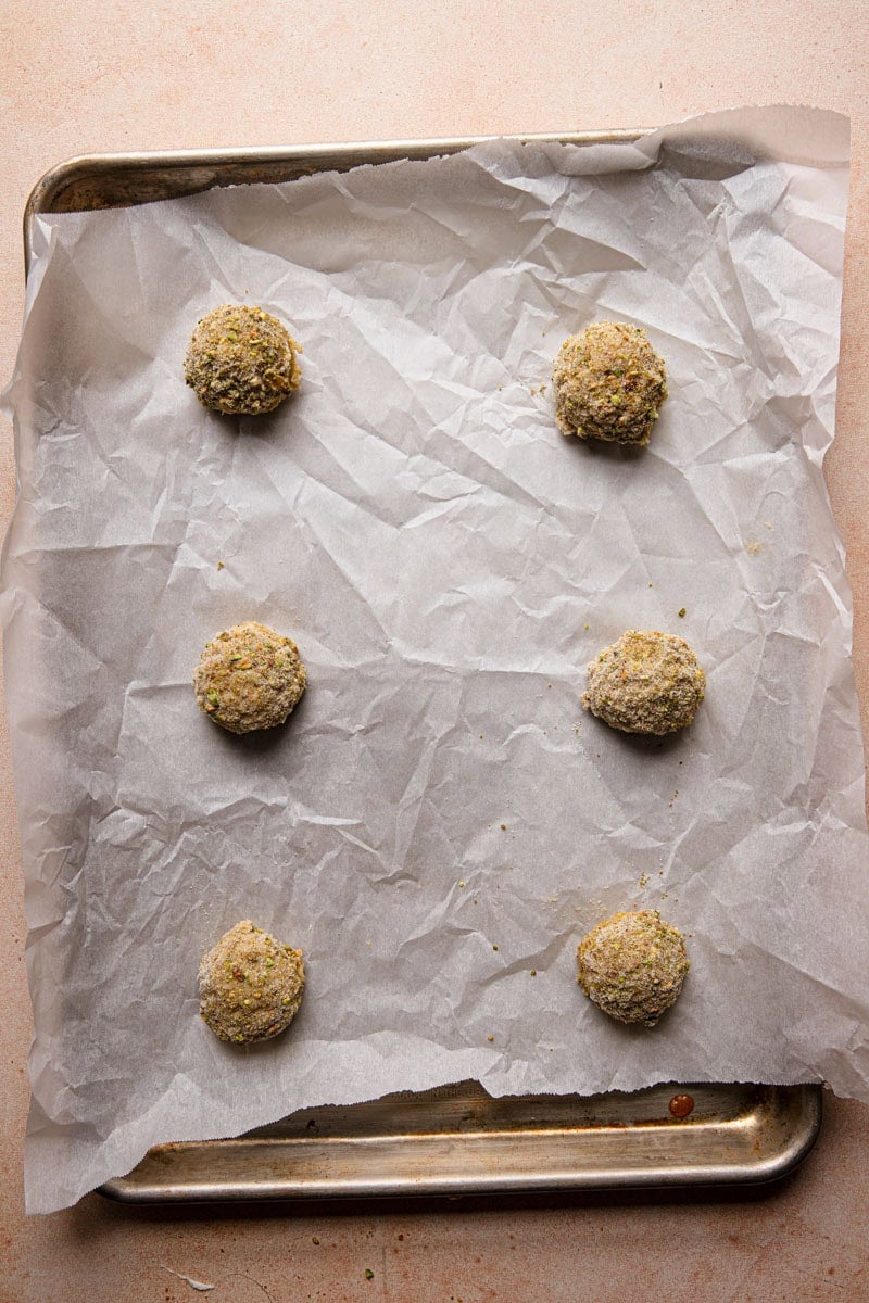 A pan lined with parchment paper topped with unbaked cookie balls, three on each side.