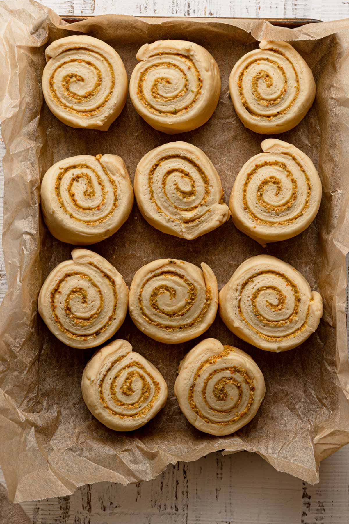Sliced unbaked swirled pastries in a pan lined with parchment paper.