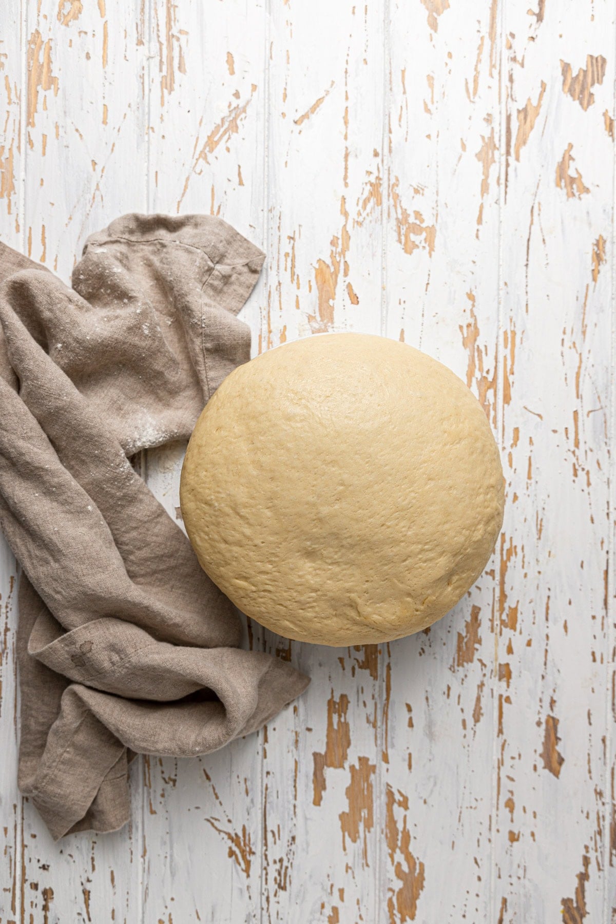 A bowl with proofed dough, a kitchen towel next to it.