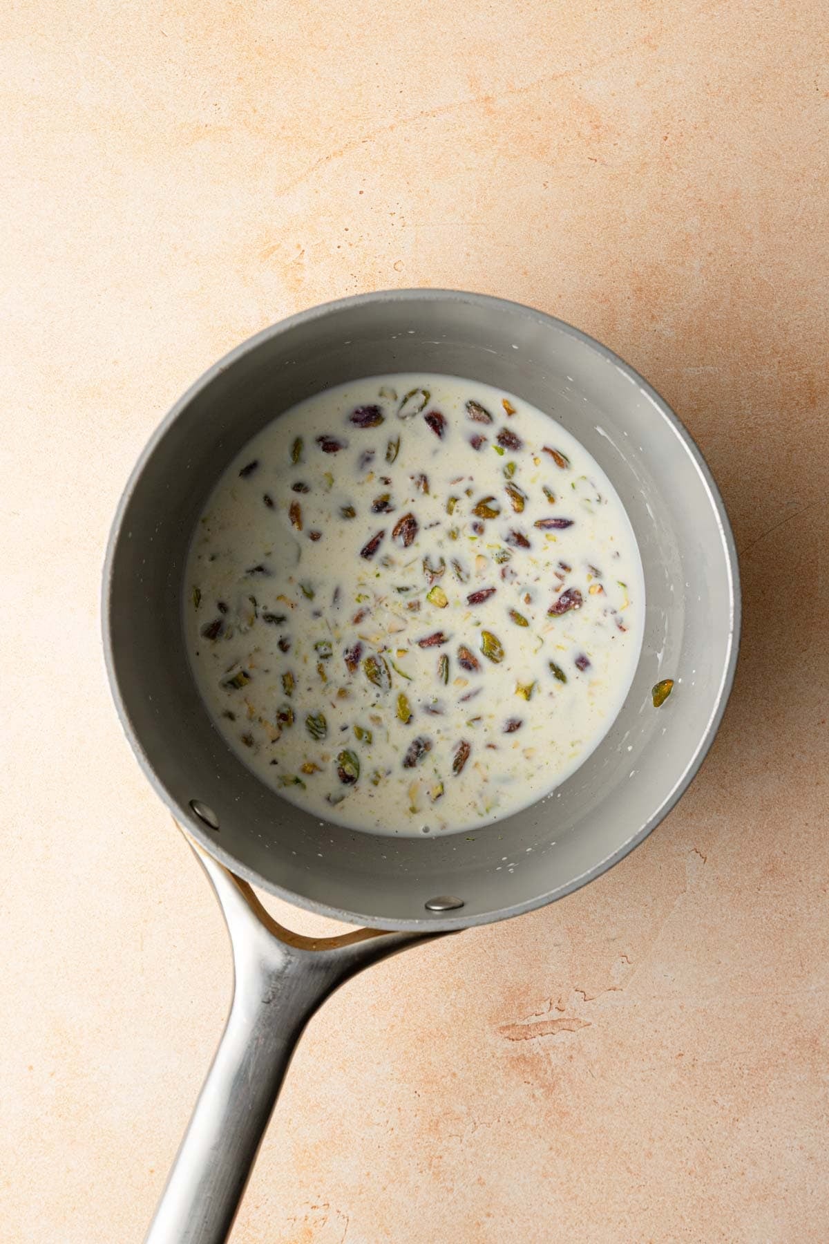 A sauce pan with milk and chopped pistachios.