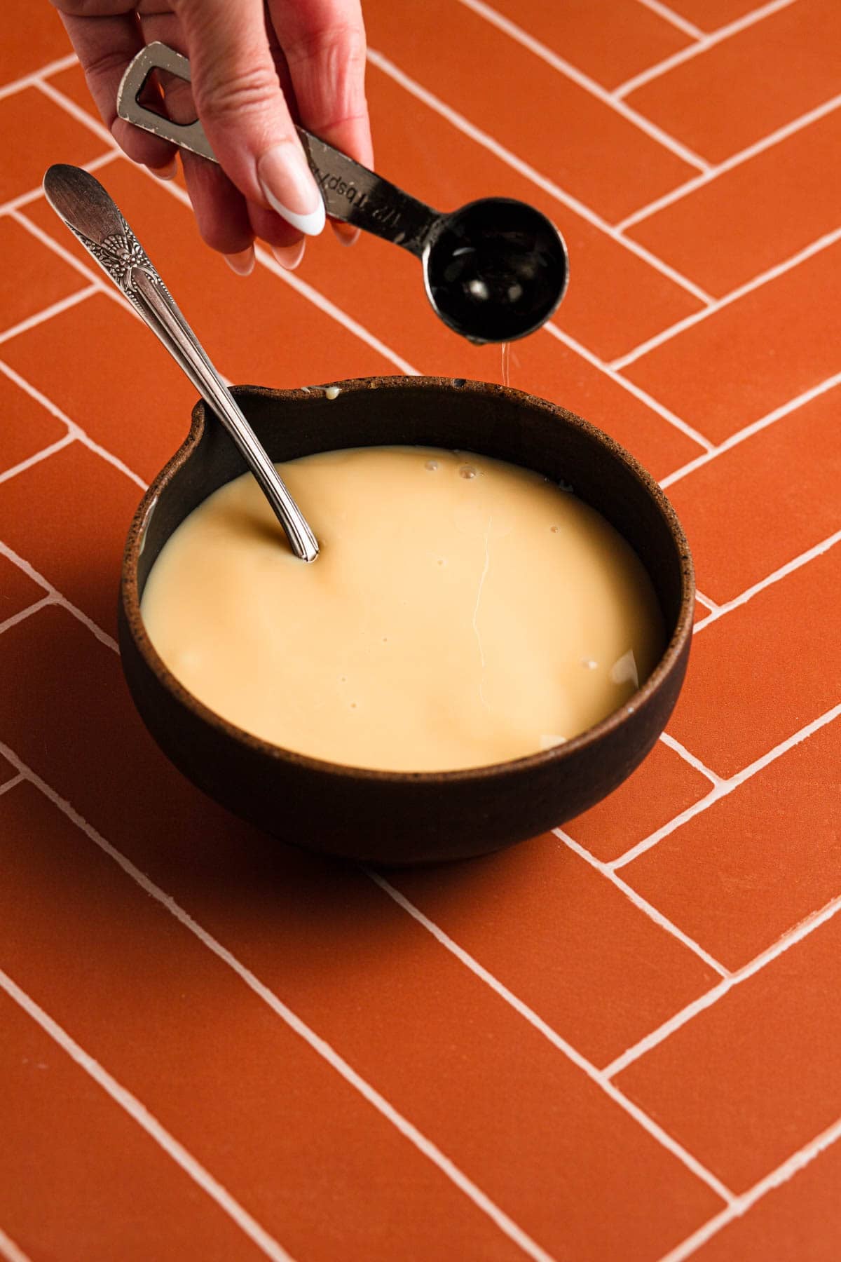 Adding extract to a bowl with sweetened condensed milk.
