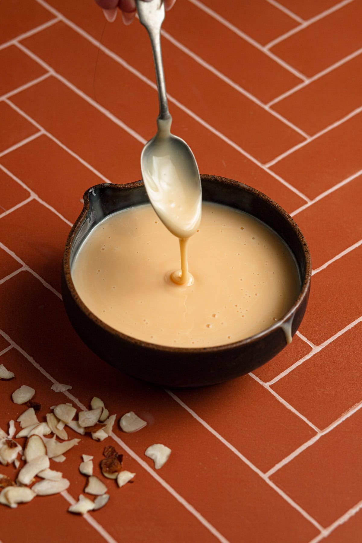 Almond Glaze in a bowl with a spoon and sliced almonds.