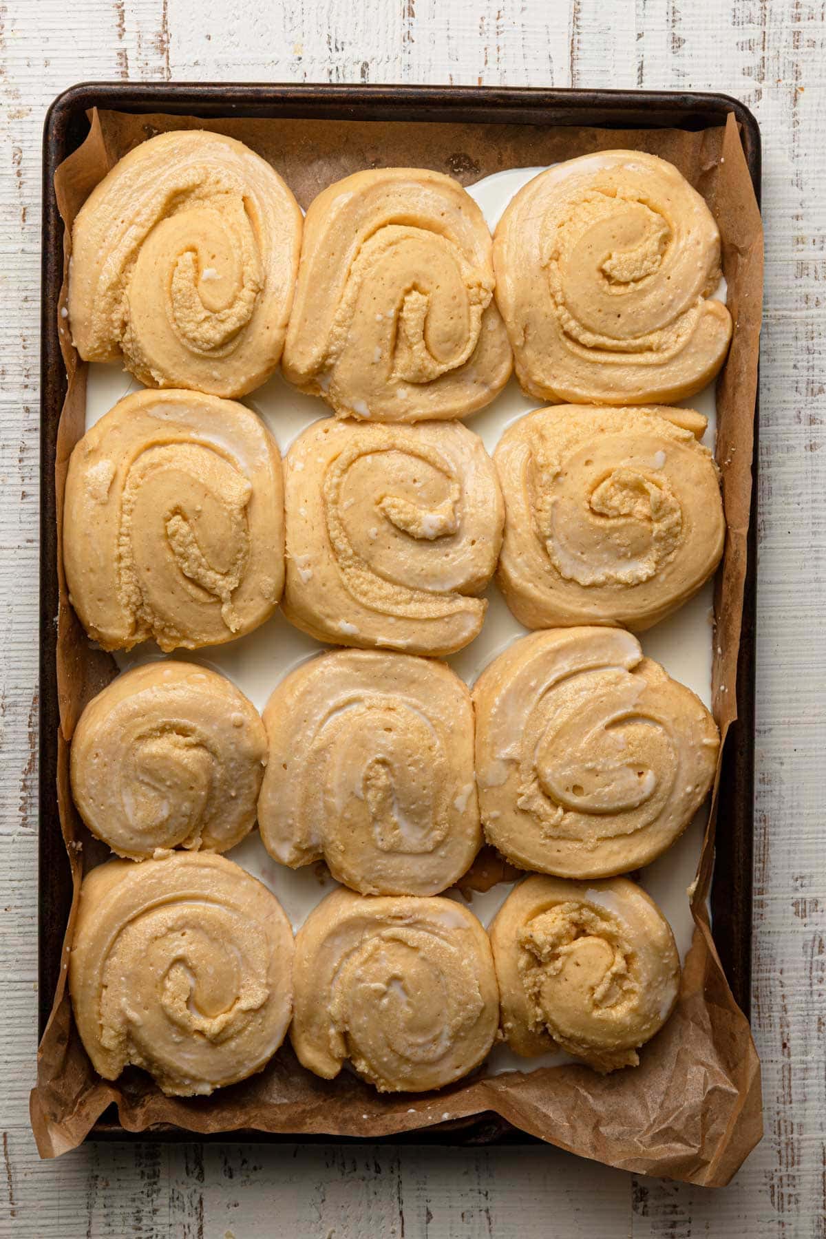 A pan with unbaked swirled dough filled with cream, and milk in between the gaps.