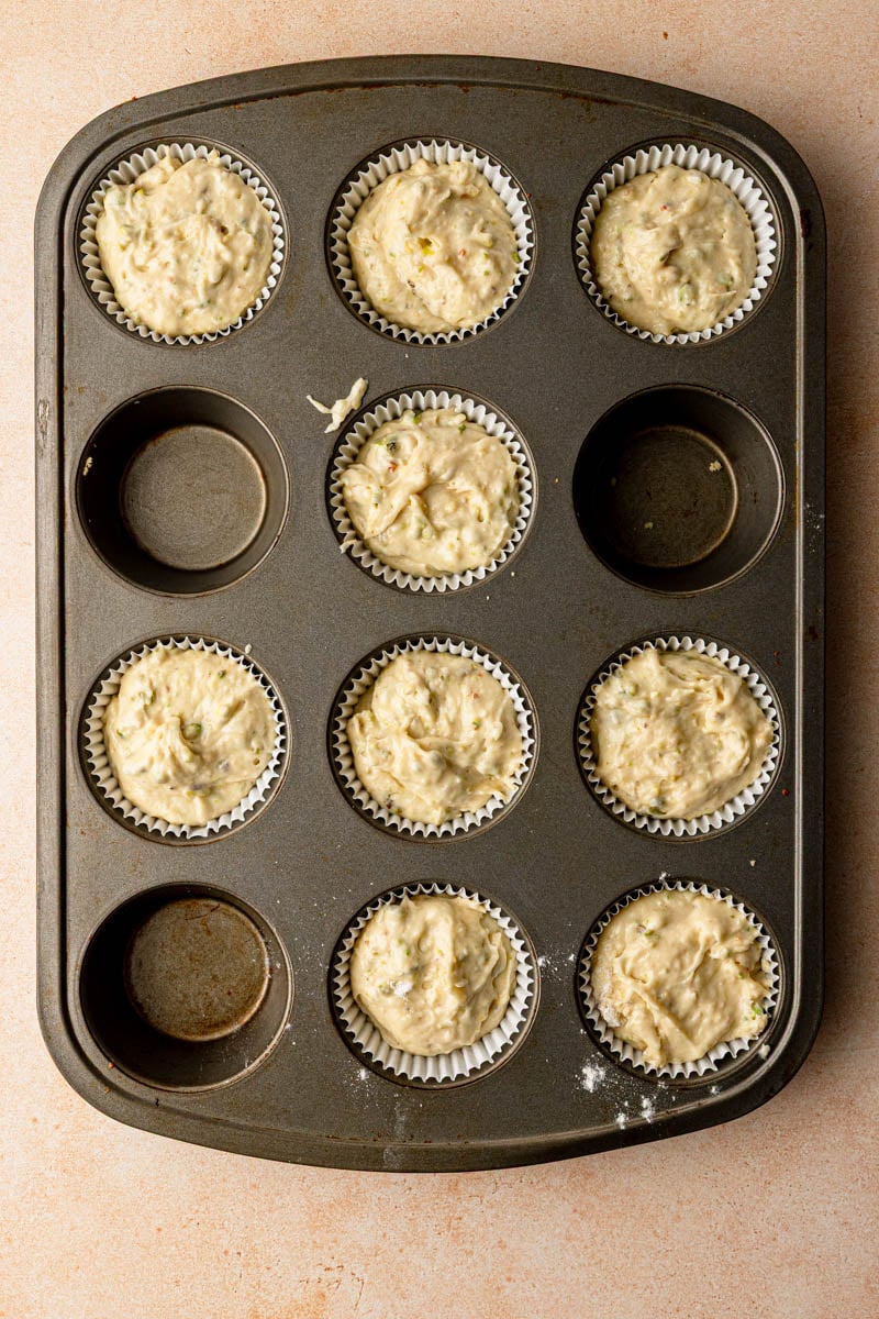 Cupcake pan with cupcakes liners and unbaked pistachio cupcakes batter.