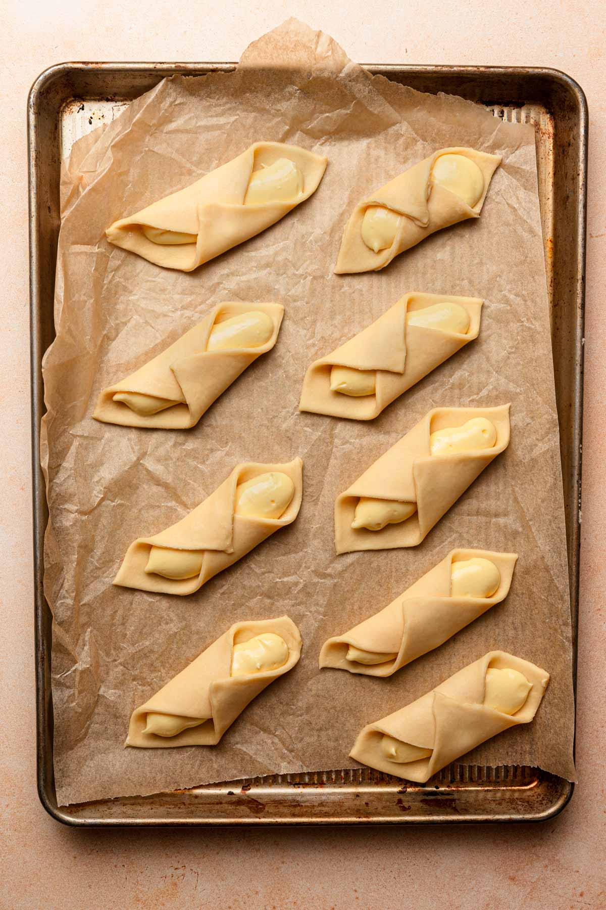A pan lined with parchment paper, topped with unbaked cheese pastires.