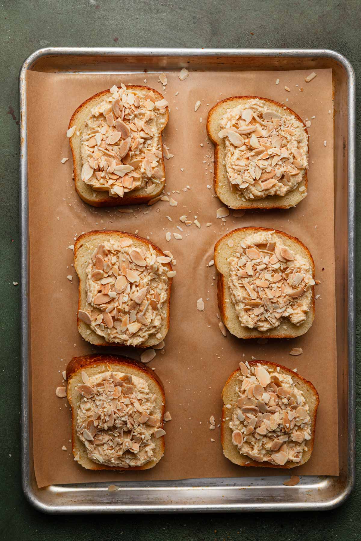 Brioche slices on a baking sheet with parchment paper spread with almond cream and sprinkled with almond.