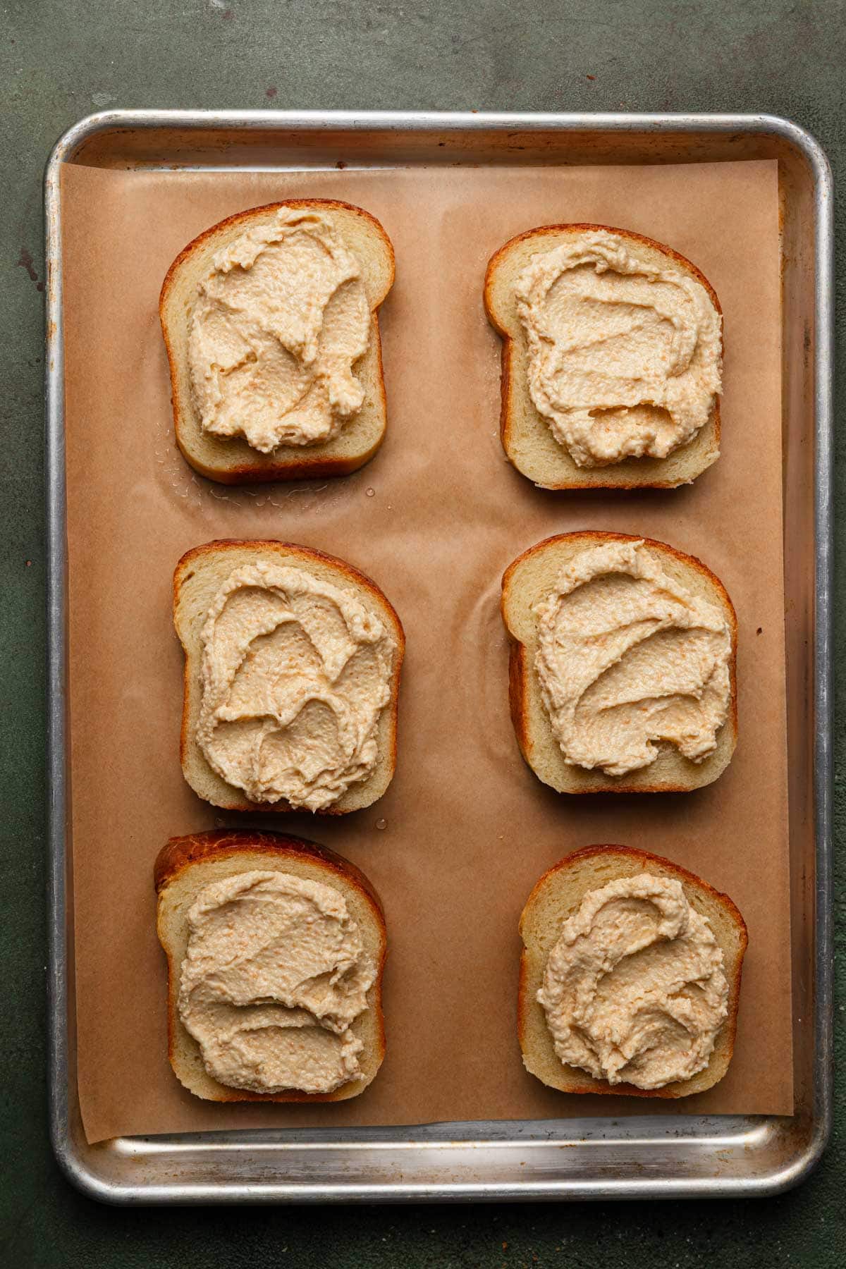 Brioche slices on a baking sheet with parchment paper spread with almond cream.