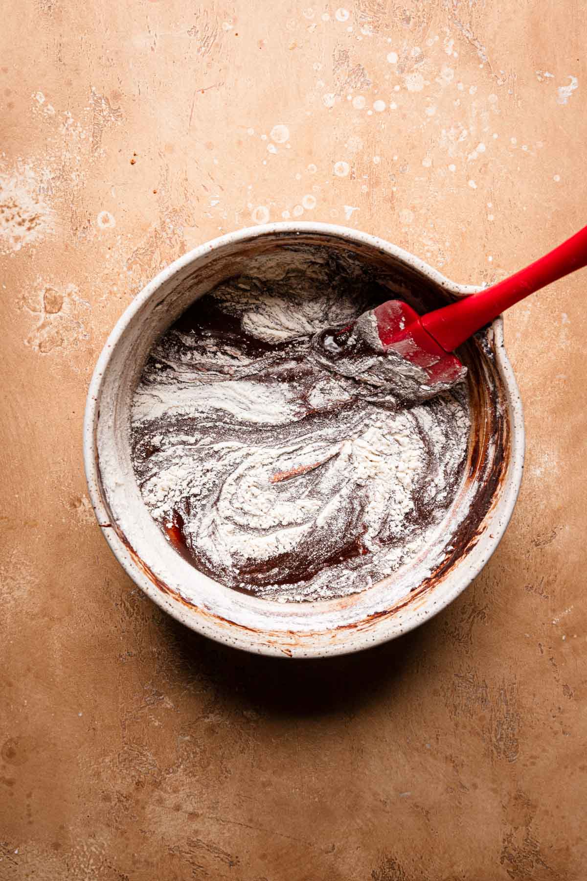 a bowl with melted chocolate and a spatula folding flour.