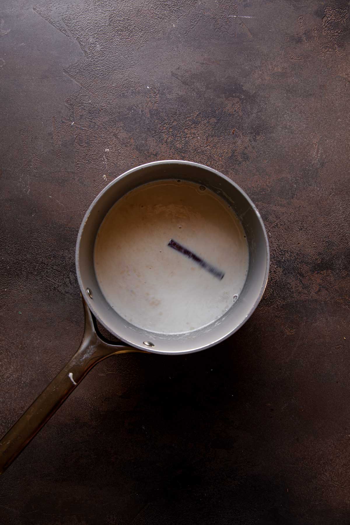 A sauce pan with milk and a cinnamon stick.