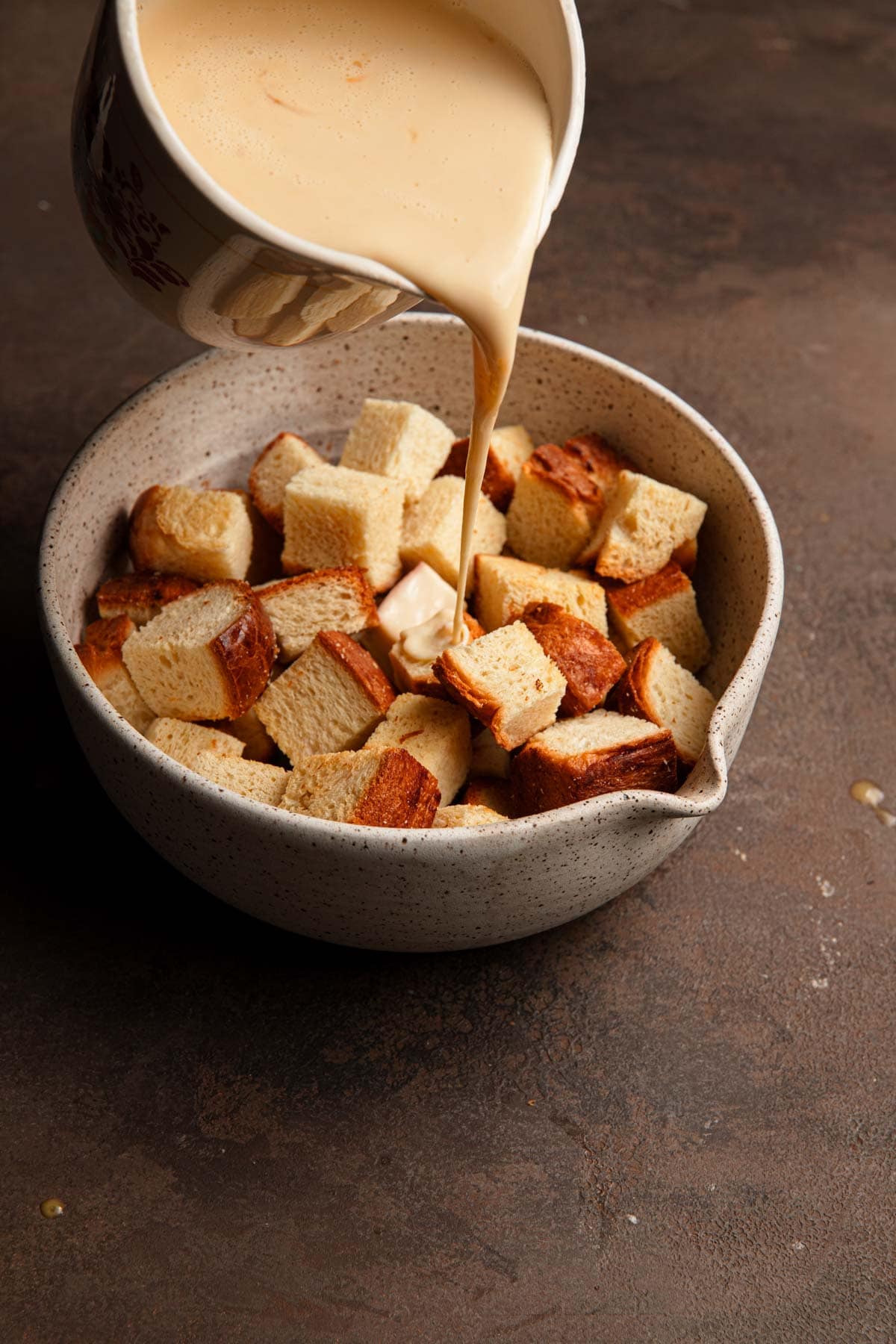 Pouring custard over bread cubes.