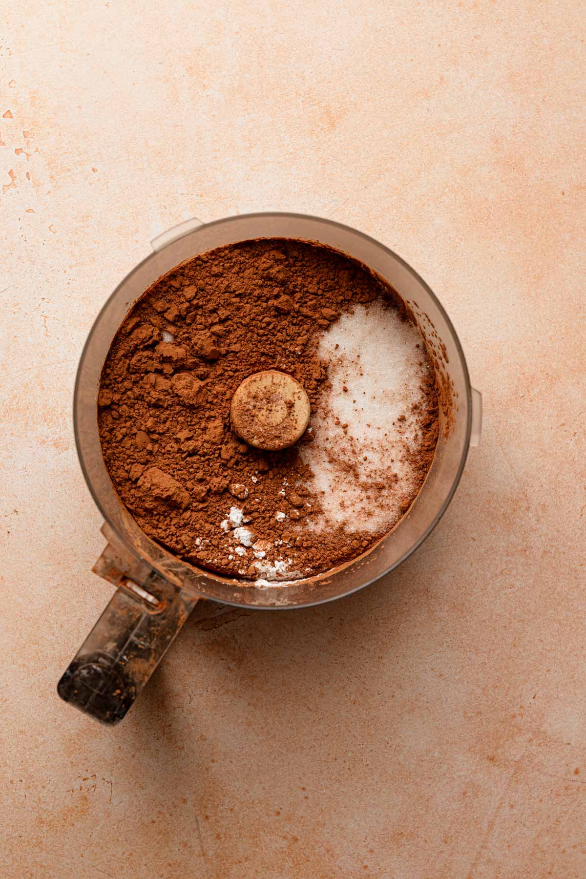 A food processor bowl with sugar and cocoa powder.