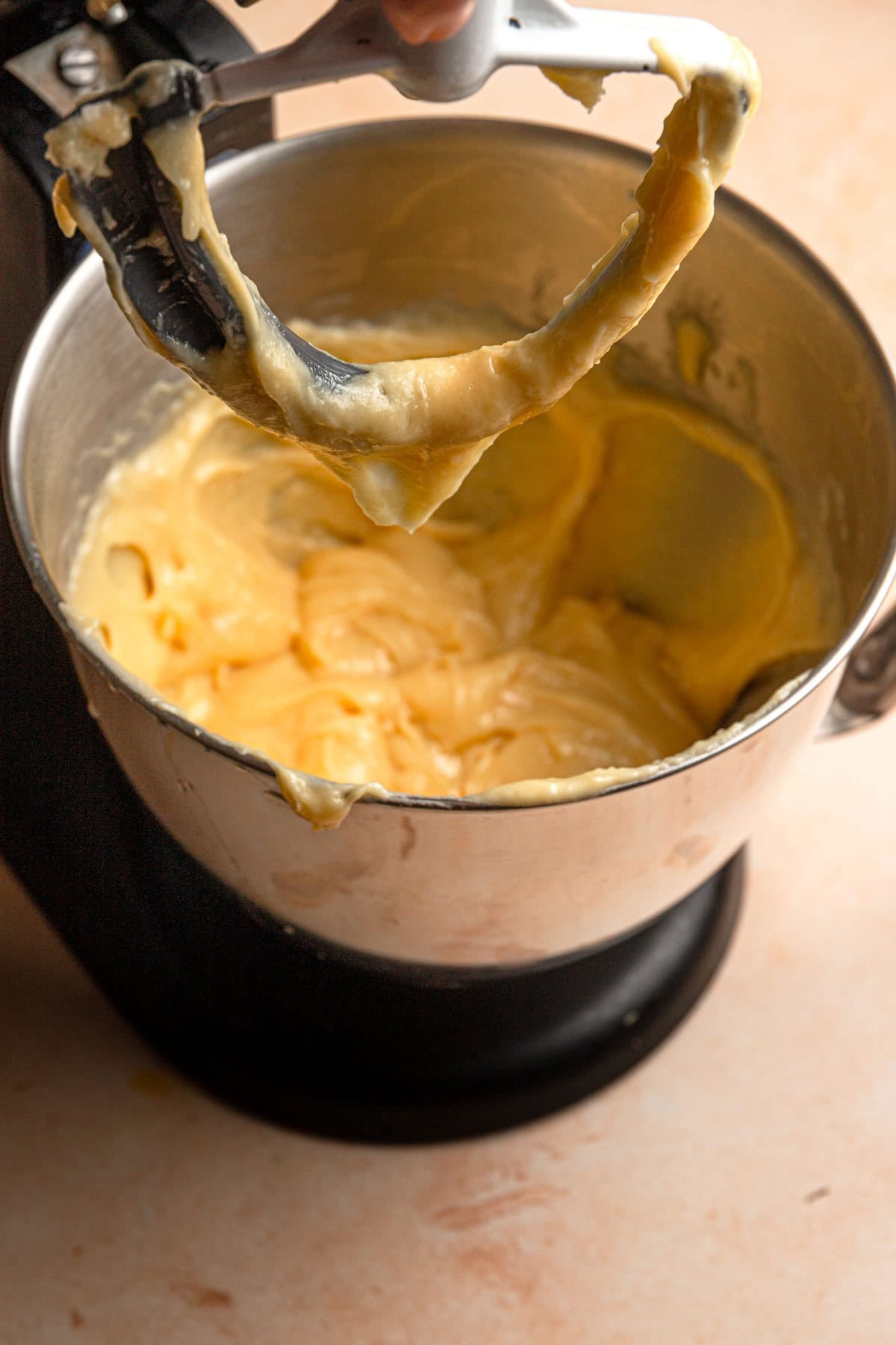 Choux paste in a stand mixer bowl hanging over a paddle attachment shaping v.