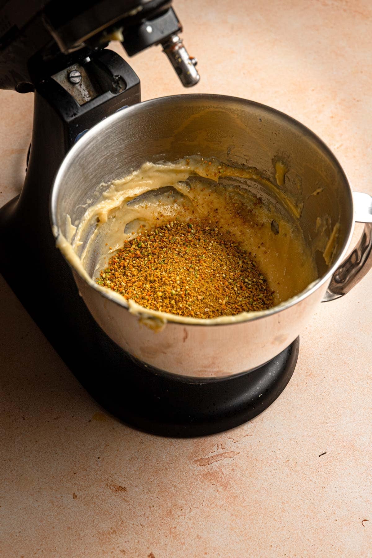 A stand mixer bowl with choux paste and ground pistachios.