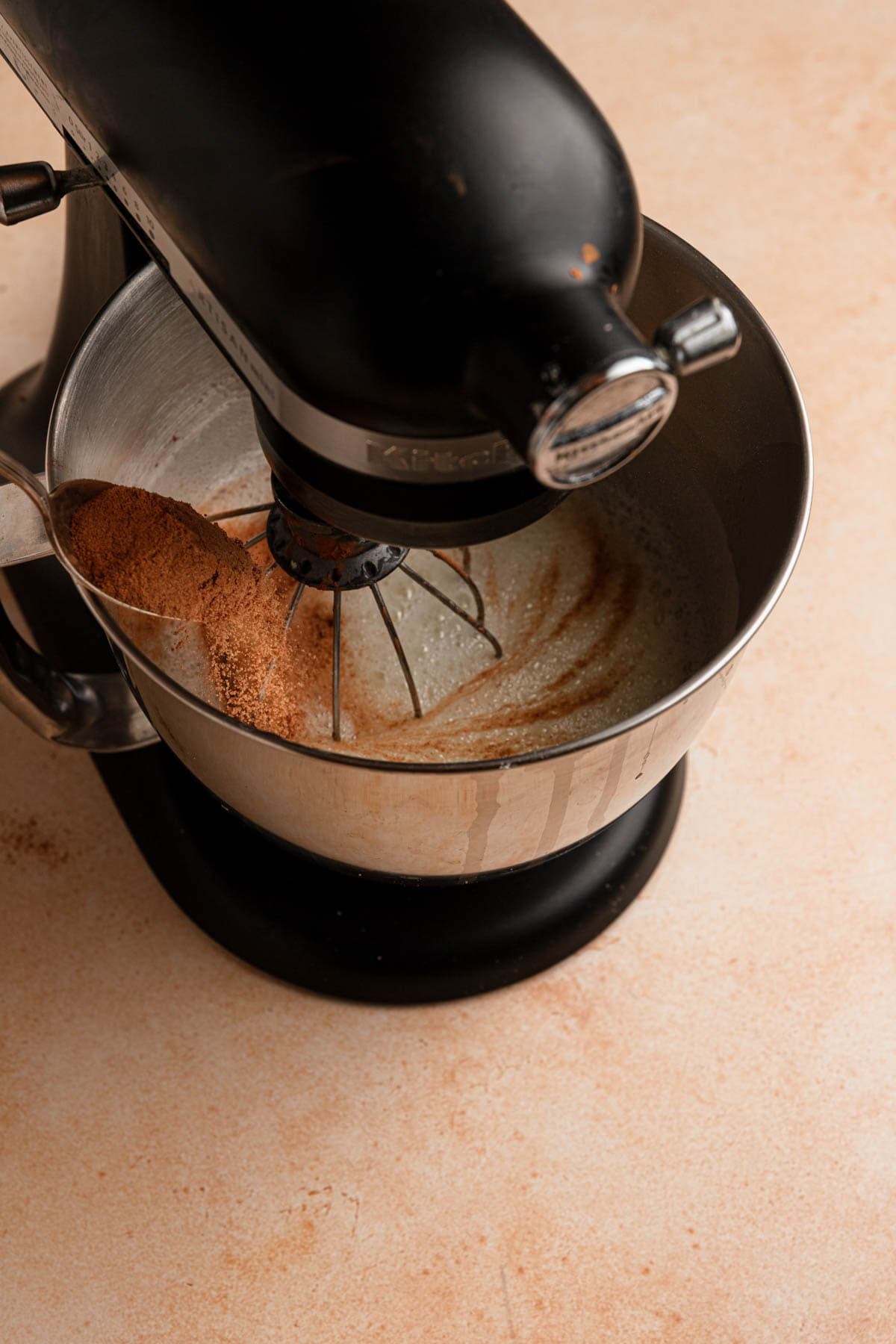 Gradually adding cocoa-sugar into egg whites while mixing in a stand mixer.