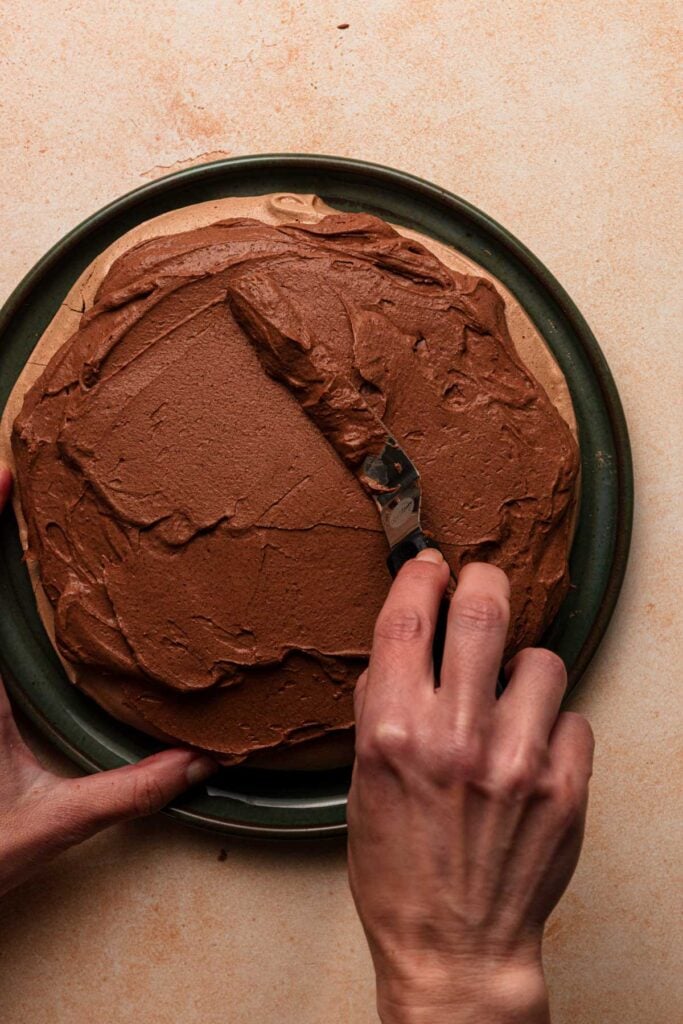 A hand spreading chocolate mousse over a chocolate meringue pieces.