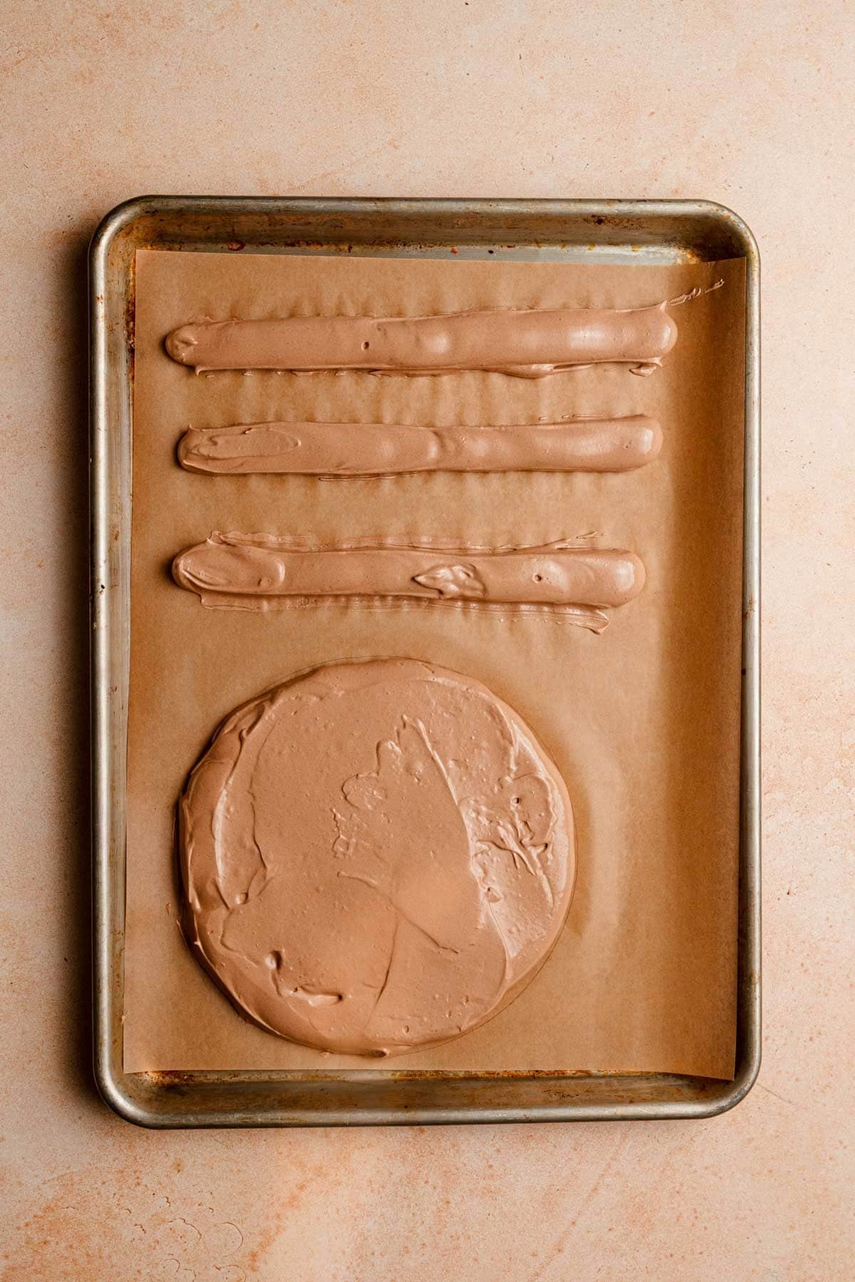 A baking sheet lined with parchment paper topped with a meringue disk and logs.