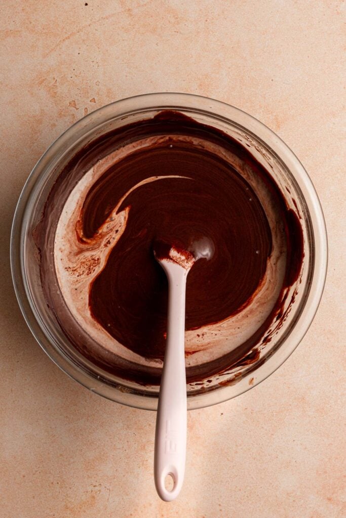 A bowl with smooth chocolate ganache and cream with a spatula.
