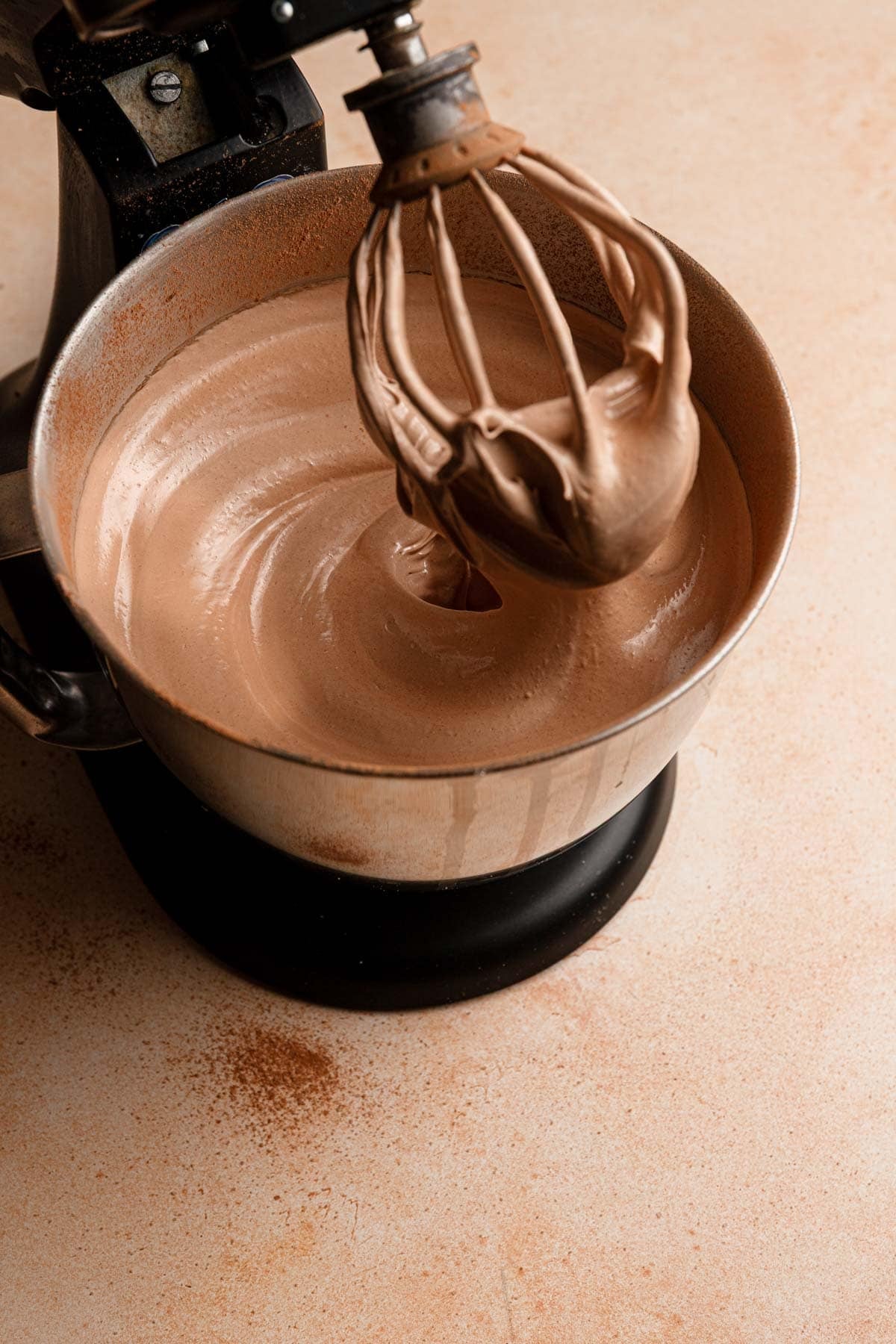 A stand mixer with a bowl filled with chocolate meringue and a whisk attachment.