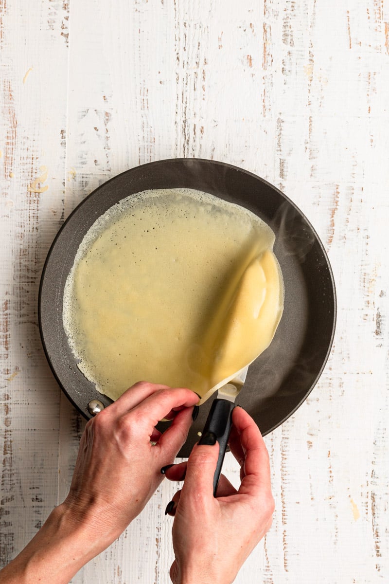 Hands turning over crepe using an offset spatula.