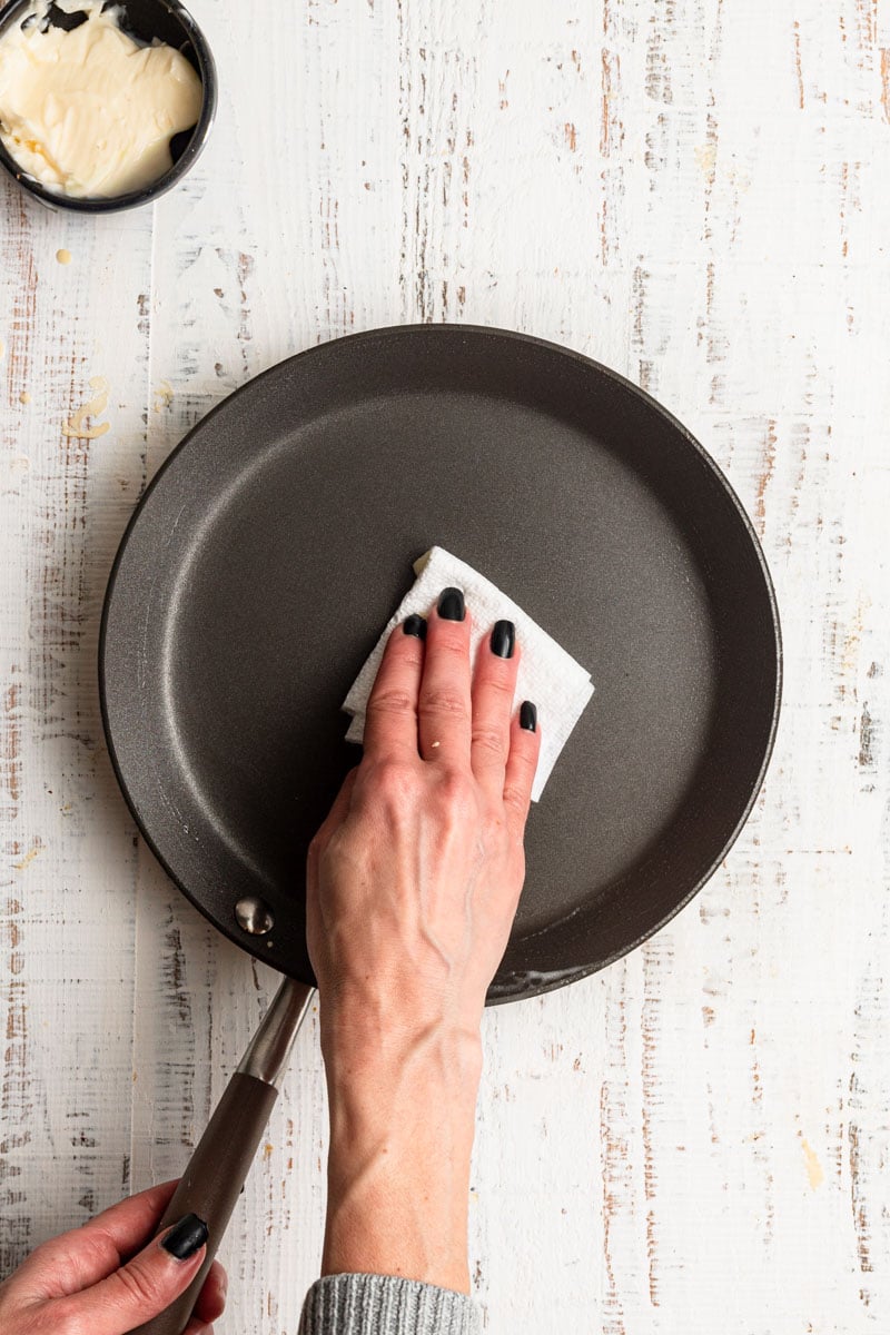 Hand greasing a skillet using a paper towel dipped in butter.