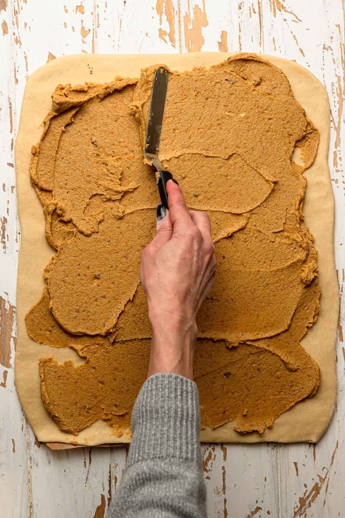 A hand spreading orange butter over rolled dough.