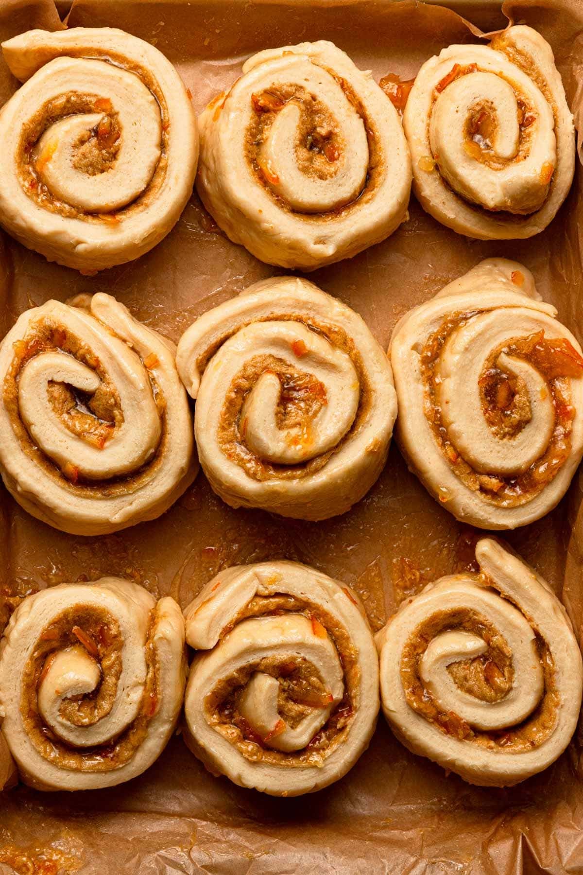 Unbaked swirled orange rolls in a pan.
